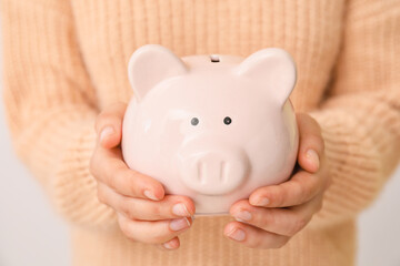 Woman with piggy bank on light background, closeup