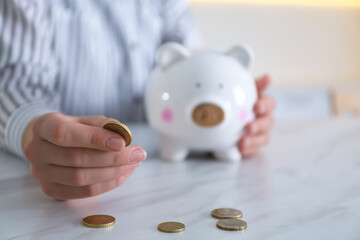 Woman with piggy bank and coin at marble table indoors, closeup