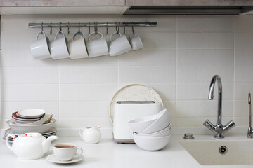 Fototapeta na wymiar White dishes: a tray, cups, plates, dishes, bowls, a toaster against the background of white kitchen trimmed with ceramics