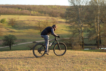 Fototapeta premium Sports brutal bearded guy on a modern mountain bike. Cyclist on the green hills in the spring.