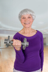 Happy charming beautiful elderly woman is doing exercise with a dumbbell. Exercising gymnastics for health in the fitness room. Sports training