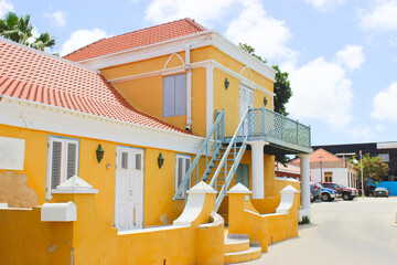 Yellow house with parking. Two flors of this house and grey road, Few cars and blue sky. Tropical country and island Aruba August 2104