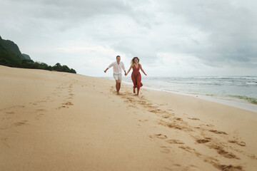 Girl and guy run along the ocean holding hands