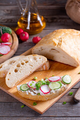 Ciabatta with curd cheese, fresh radish, cucumber on a wooden cutting board - concept of healthy fitness breakfast or snack