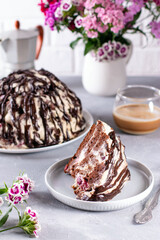 Dessert, sliced homemade cake with chocolate biscuit, cherry and cream of sour cream and whipped cream on a white plate on a light concrete background.