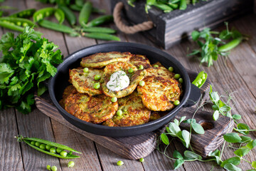 Vegetarian zucchini fritters or pancakes, served with greek yogurt, green peas and green onion in frying pan on a table