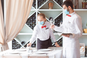 Obraz premium the waiter serves a table in a cafe in a protective mask.