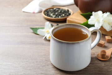 Obraz na płótnie Canvas Cup of tea and fresh jasmine flowers on wooden table. Space for text