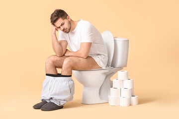Young man with rolls of paper sitting on toilet bowl against color background