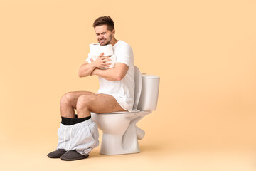 Young man with rolls of paper sitting on toilet bowl against color background