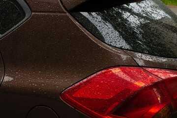 Close-up of the red taillight of a brown modern car with raindrops