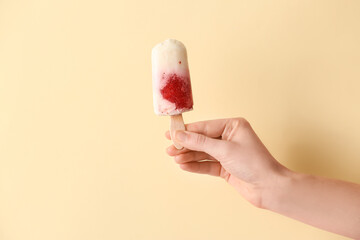 Hand with tasty strawberry ice cream on color background