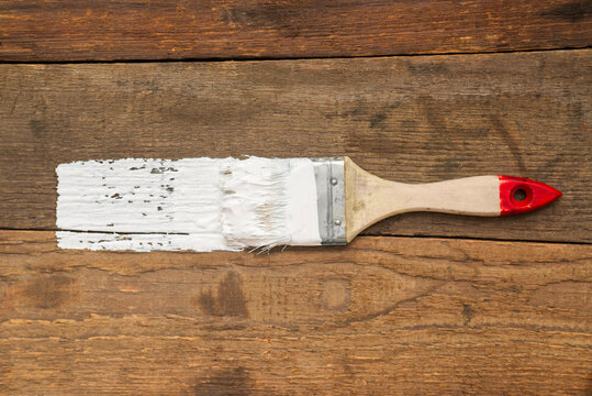 Brush with white paint on a wooden background. There is a place for advertising or inscription