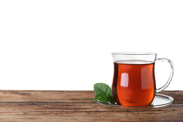 Glass cup of aromatic black tea and green leaves on wooden table against white background. Space for text