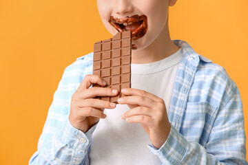 Cute little boy eating chocolate on color background