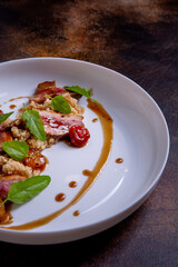 A quinoa, teriyaki sauce and confit tomatoes on a white plate against a dark background. Master class in the kitchen. The process of cooking. Dish from the restaurant menu. European cuisine. Close-up