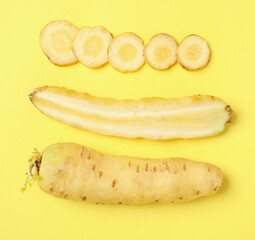 Whole and cut raw white carrots on yellow background, flat lay