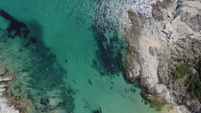 Mediterranean Greek landscape beach drone shot. Aerial top view of Sithonia Chalkidiki peninsula with panning from rocky coastal to crystal clear waters & sea beds with umbrellas.