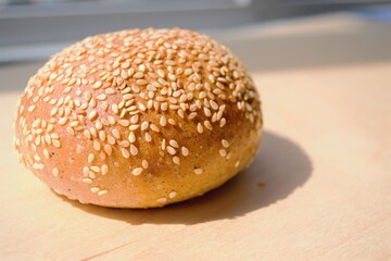 Homemade rye bun with sesame seeds on a wooden surface in the bright rays of the daylight