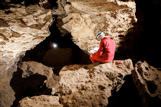 Man walking and exploring dark cave with light headlamp underground. Mysterious deep dark, explorer discovering mystery moody tunnel looking on rock wall inside.