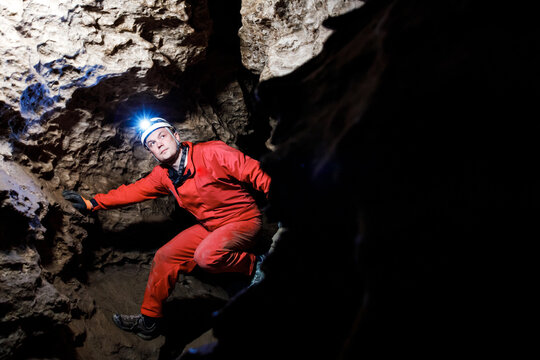 Man walking and exploring dark cave with light headlamp underground. Mysterious deep dark, explorer discovering mystery moody tunnel looking on rock wall inside.