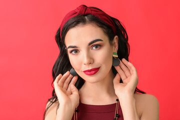 Beautiful young woman wearing stylish jewelry on color background