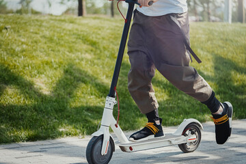 Close up of man riding electric kick scooter at beautiful park landscape.