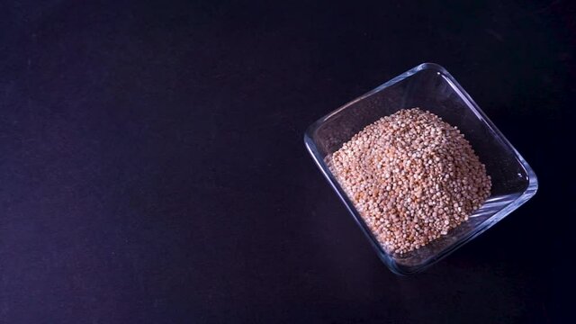 Quinoa seca vertida sobre recipiente de cristal en mesa negra