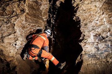 Speleologist descend by the rope in the deep vertical cave tunnel. Cave man hanging over abyss. View from the top og the tunnel.