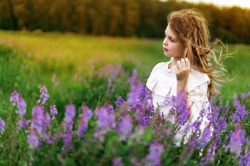 Fototapeta na wymiar A little girl in a white dress with beautiful flowers in the field in summer. Concept of happy childhood. Copy space for text