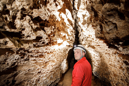Man walking and exploring dark cave with light headlamp underground. Mysterious deep dark, explorer discovering mystery moody tunnel looking on rock wall inside.