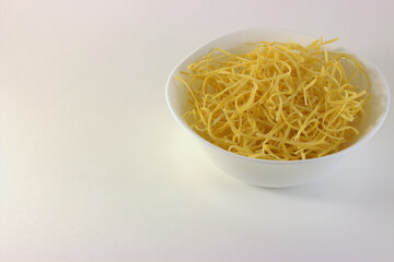 Dry homemade noodles in a white deep plate on a white background. There is copyspace nearby