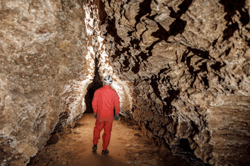 Obraz na płótnie Canvas Man walking and exploring dark cave with light headlamp underground. Mysterious deep dark, explorer discovering mystery moody tunnel looking on rock wall inside.