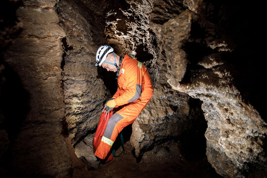 Man walking and exploring dark cave with light headlamp underground. Mysterious deep dark, explorer discovering mystery moody tunnel looking on rock wall inside.