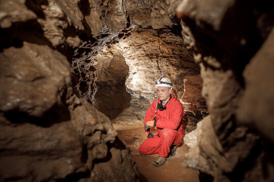 Man walking and exploring dark cave with light headlamp underground. Mysterious deep dark, explorer discovering mystery moody tunnel looking on rock wall inside.
