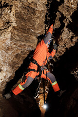 Naklejka premium Speleologist descend by the rope in the deep vertical cave tunnel. Cave man hanging over abyss. View from the top og the tunnel.