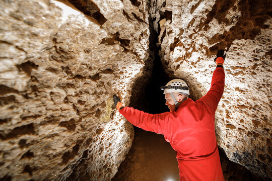 Man walking and exploring dark cave with light headlamp underground. Mysterious deep dark, explorer discovering mystery moody tunnel looking on rock wall inside.