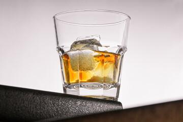 a glass of whiskey with ice stands on the corner of the bar in the center of the frame on a light gray background. close up, bot view. horizontal orientation