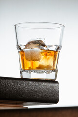 a glass of whiskey with ice stands on the corner of the bar counter on a light gray background. close up, side view, copy space. vertical orientation