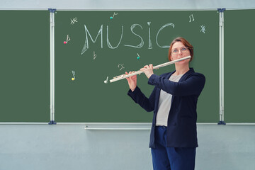 A music teacher with a flute stands next to a blackboard in a school classroom. Learning to play wind musical instruments