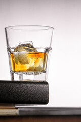 a glass of whiskey with ice stands on the corner of the bar counter on a light gray background. close up, bot view, copy space. vertical orientation
