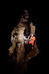 Man walking and exploring dark cave with light headlamp and map in his hand underground. Mysterious deep dark, explorer discovering mystery moody tunnel looking on rock wall inside.