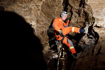 Obraz premium Speleologist descend by the rope in the deep vertical cave tunnel. Cave man hanging over abyss. View from the top og the tunnel.