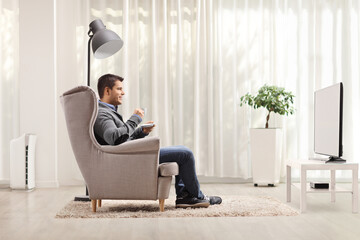 Man in an armchair drinking coffee and watching tv