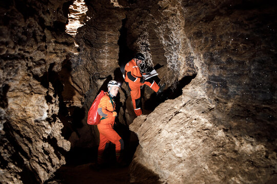 Two men, strong physique, explore the cave. Men dressed in special clothes to pass through the cave and stopped, looking at the map