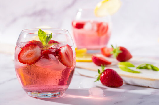 Cold pink strawberry flavoured jin and tonic garnished with fresh fruits and mint leaves.