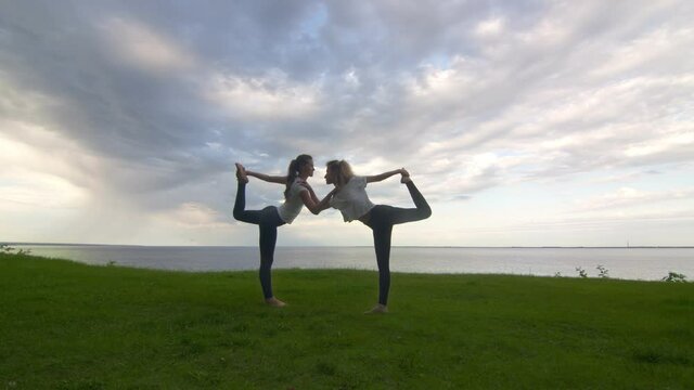 Two women in activewear pposing on the camera and showing yoga Lord of the Dance pose