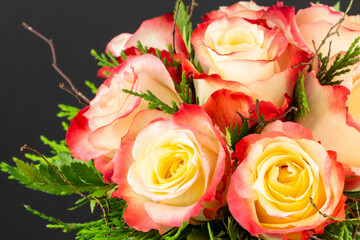 Yellow and red bic-olured roses arranged with branches and fresh greens, and copy space.
