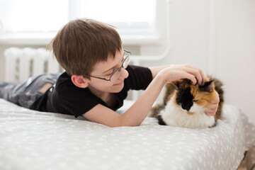 Boy playing with cat on bed. Staying at home. Pet therapy. Spending a time & feeding a pet cat. Happy time together with friend pet. Excited Smiling boy Enjoying With His cat. Social distancing