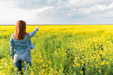 Fototapeta premium Woman pointing to the horizon on blossoming field